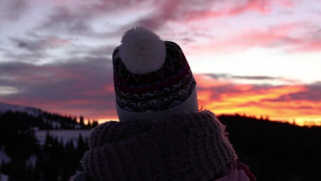 Silhouette of a young woman in winter clothing holding a phone in her hands taking pictures of a beautiful sunset