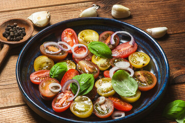 Salad with halves of red and yellow tomatoes cherry with basil, topping balsamic sauce on white plate