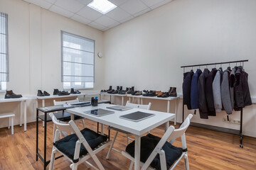 A showroom with a table for visitors, clothes on a hanger and shoes on the shelves.