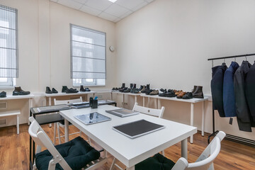A bright showroom with a table for visitors and hangers with clothes and shelves with shoes.