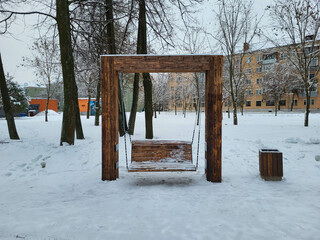 Wooden swing outside in winter under a thick layer of snow. The theme of winter cold and entertainment.