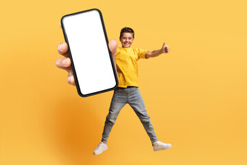 Cute caucasian boy jumping in the air, showing big phone