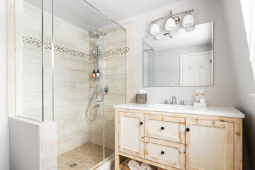 A bathroom with a wood cabinet, white marble countertop, and a brown tiled walk-in shower. No...