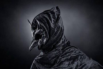 Creepy figure with animal horned skull over dark misty background
