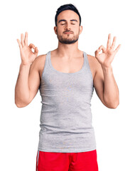Young handsome man wearing swimwear and sleeveless t-shirt relaxed and smiling with eyes closed doing meditation gesture with fingers. yoga concept.