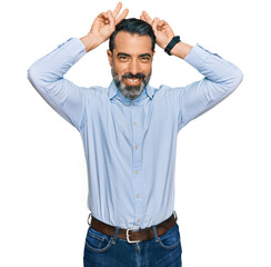 Middle aged man with beard wearing business shirt posing funny and crazy with fingers on head as bunny ears, smiling cheerful