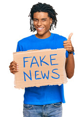 Young african american man holding fake news banner smiling happy and positive, thumb up doing...