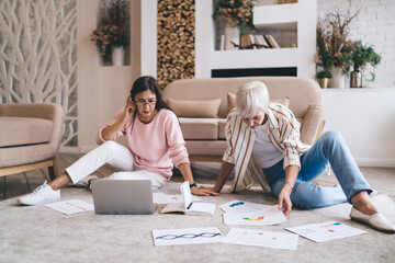 Concentrated diverse women working with diagrams remotely sitting on floor