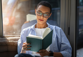 Engrossed young woman with glasses deeply focused on reading a book