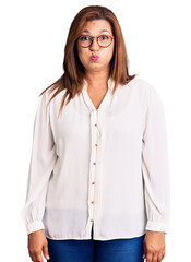 Middle age latin woman wearing casual clothes and glasses puffing cheeks with funny face. mouth inflated with air, crazy expression. - obrazy, fototapety, plakaty