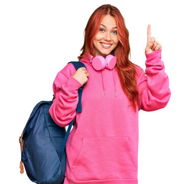 Young redhead woman holding student backpack and books surprised with an idea or question pointing finger with happy face, number one