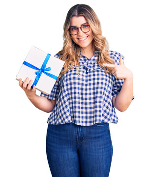 Young caucasian woman holding gift pointing finger to one self smiling happy and proud