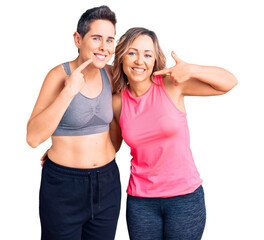 Couple of women wearing sportswear smiling cheerful showing and pointing with fingers teeth and mouth. dental health concept.