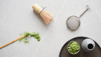 Matcha green tea powder and utensils for drink preparation: traditional bamboo spoon and whisk.