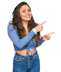 Young hispanic girl wearing casual clothes smiling and looking at the camera pointing with two hands and fingers to the side.