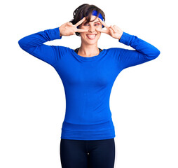 Beautiful young woman with short hair wearing training workout clothes doing peace symbol with fingers over face, smiling cheerful showing victory