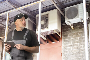 Air conditioners installation wizard. Man electrician with tablet. External air conditioning units...