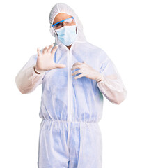 Young hispanic man wearing doctor protection coronavirus uniform and medical mask disgusted expression, displeased and fearful doing disgust face because aversion reaction. with hands raised