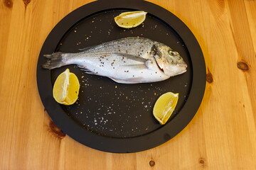 Raw fresh fish dorado with lemon and spices on wooden table. Top view