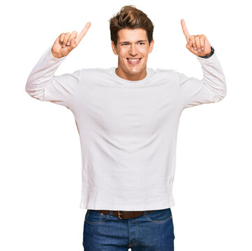 Handsome caucasian man wearing casual white sweater smiling amazed and surprised and pointing up with fingers and raised arms.