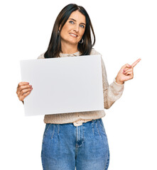 Middle age brunette woman holding blank empty banner smiling happy pointing with hand and finger to the side