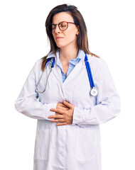 Young beautiful woman wearing doctor stethoscope and glasses with hand on stomach because indigestion, painful illness feeling unwell. ache concept.