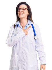 Young beautiful woman wearing doctor stethoscope and glasses cheerful with a smile of face pointing with hand and finger up to the side with happy and natural expression on face