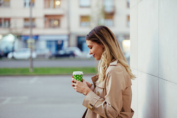 Profile of a stylish young woman on the city street looking at her coffee.