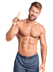 Young caucasian man standing shirtless showing and pointing up with finger number one while smiling confident and happy.