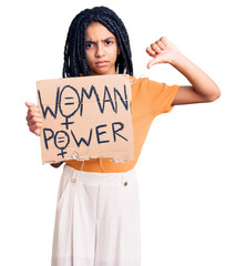 Cute african american girl holding woman power banner with angry face, negative sign showing dislike with thumbs down, rejection concept