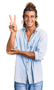 Young hispanic man wearing summer style smiling with happy face winking at the camera doing victory sign with fingers. number two.