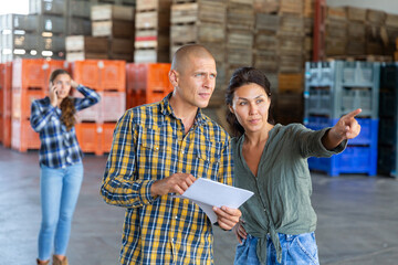 Man and woman stand inside fruit warehouse and discuss a document