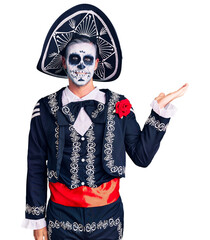 Young man wearing day of the dead costume over background smiling cheerful presenting and pointing with palm of hand looking at the camera.