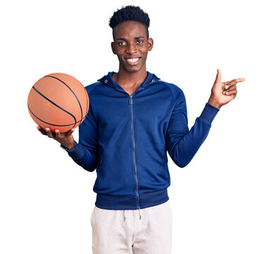 Young african american man holding basketball ball smiling happy pointing with hand and finger to the side