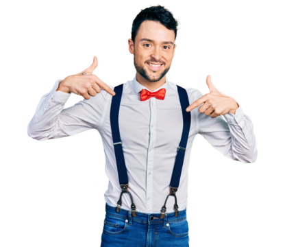 Hispanic man with beard wearing hipster look with bow tie and suspenders looking confident with smile on face, pointing oneself with fingers proud and happy.