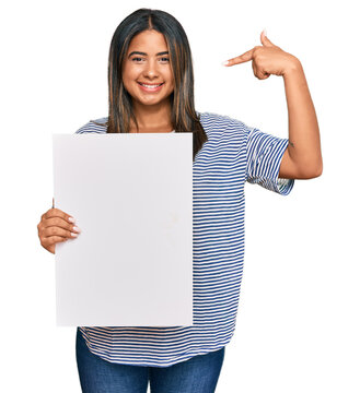 Young latin girl holding blank empty banner pointing finger to one self smiling happy and proud