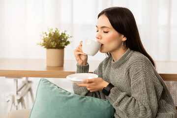 Relaxed young woman enjoying aromatic coffee at home
