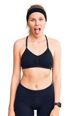 Young beautiful blonde woman wearing sportswear sticking tongue out happy with funny expression. emotion concept.