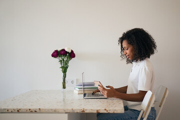 Young woman sitting at kitchen counter, drinking coffee and using laptop while relaxing at home in the morning. Education concept, distance learning, self-education, video conference class with tutor 