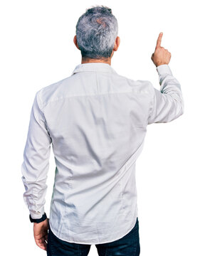 Middle age hispanic with grey hair wearing casual white shirt posing backwards pointing ahead with finger hand