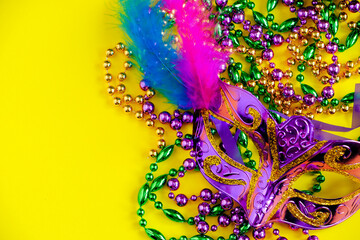 Carnival mask and beads on yellow background. Mardi Gras concept. Fat Tuesday symbol.