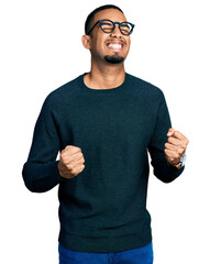 Young african american man wearing casual clothes and glasses excited for success with arms raised...