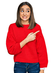 Beautiful brunette woman wearing casual winter sweater pointing aside worried and nervous with...