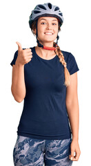 Beautiful caucasian woman wearing bike helmet doing happy thumbs up gesture with hand. approving expression looking at the camera showing success.