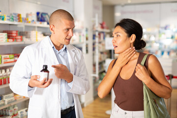 Woman complains to a pharmacist about a sore throat. Help in choosing a medicine in a pharmacy