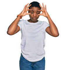 Fototapeta premium Young african american woman wearing casual white t shirt trying to open eyes with fingers, sleepy and tired for morning fatigue