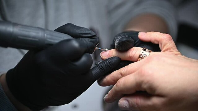 Closeup master manicurist uses professional electric machine to remove nail polish hands during hardware manicure in a beauty salon. The process of removing gel shellac polish from client's nails