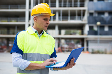 Portrait of positive man architect standing with laptop in construction site outdoors