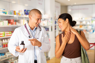 Oriental woman talking with pharmacist in drugstore and complaining about pain in her neck.