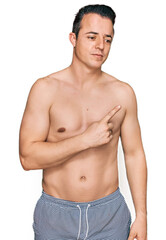 Fototapeta premium Handsome young man wearing swimwear shirtless pointing with hand finger to the side showing advertisement, serious and calm face